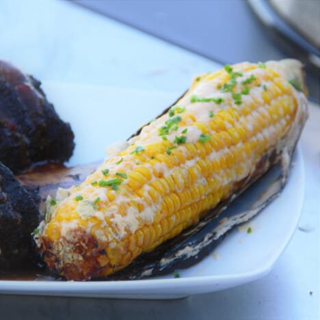 A single cob of Mexican street corn sits on a dinner plate garnished with fresh chives.