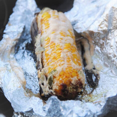 Mexican street corn just after unwrapping the foil, showing the melted cheese slather.
