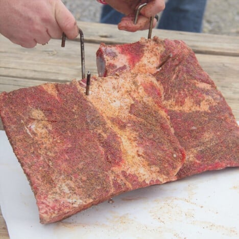 Two racks of beef ribs being prepared on a white chopping board with the hooks added.