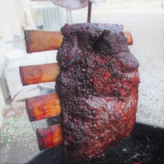 A rack of beef ribs being lifted from the smoker by the hook.
