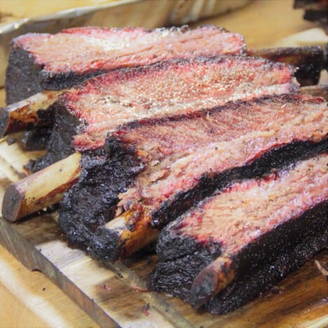 A wooden chopping board with cooked beef ribs cut into single bone serving portions.