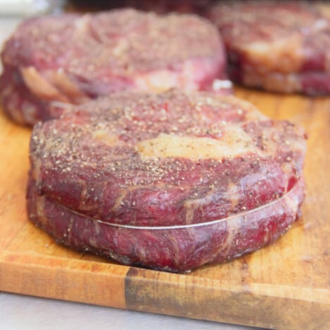 A raw steak is siting on a chopping board bound in butchers twine and seasoned.