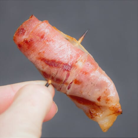 A single prosciutto-wrapped Scallop being held up by its toothpick.