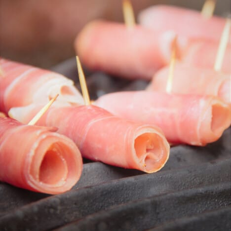 Raw prosciutto-wrapped scallops have just been placed on the grill to cook.