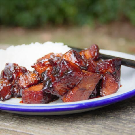 Looking into a white plate with glazed Chinese braised pork belly cubes and white rice.