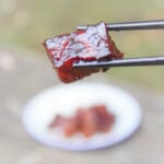 A pair of black chopsticks holds up a single cube of Chinese braised pork belly.