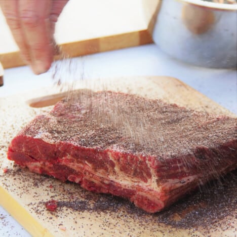 Trimmed beef ribs are having a coffee rub sprinkled over them by hand.