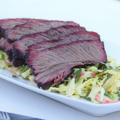 A white serving platter with sliced beef ribs laid over a salad.