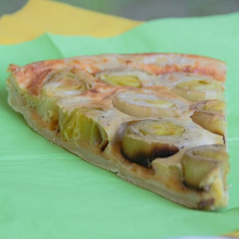 A single slice of leek tart tartin sits on a piece of green paper.