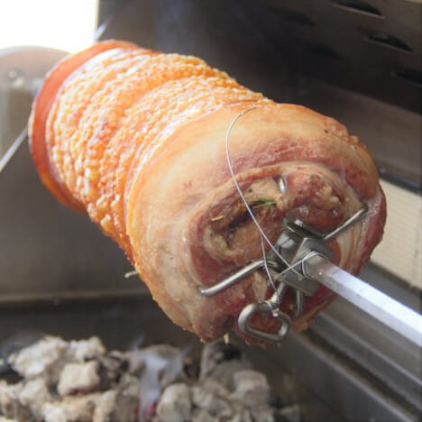 A golden-skinned pork porchetta nearing finish on a barbecue rotisserie.