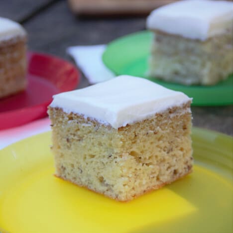 Three squares of banana cake sit on a red, yellow, and green plate.