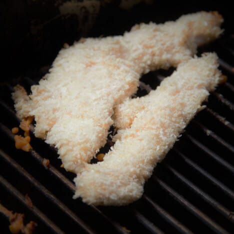 Two crumbed flathead tails sitting on a grill grate.
