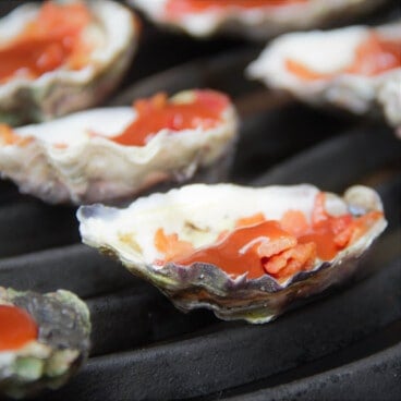 Close up of oysters Kilpatrick on the grill cooking.