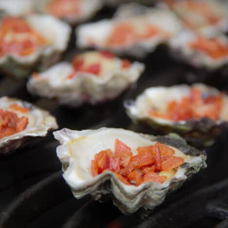 Oysters on a grill with diced bacon in them.