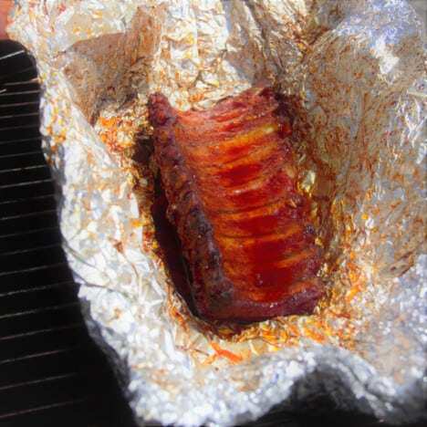 A pork rib sitting in foil after being slow cooked in the smoker.