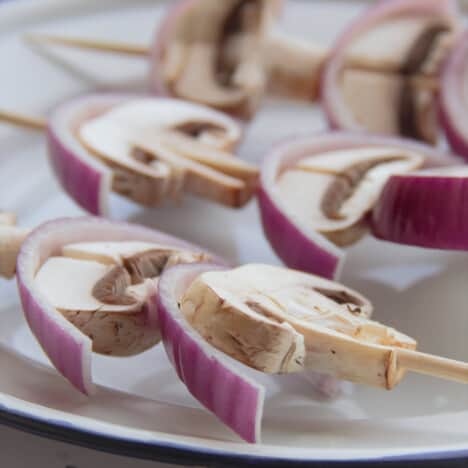 Prepared mushroom and red onion skewers on a plate ready to be cooked.