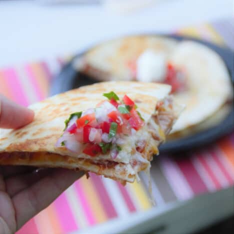 A close up of a wedge of a pulled pork quesadilla with pico de gallo.