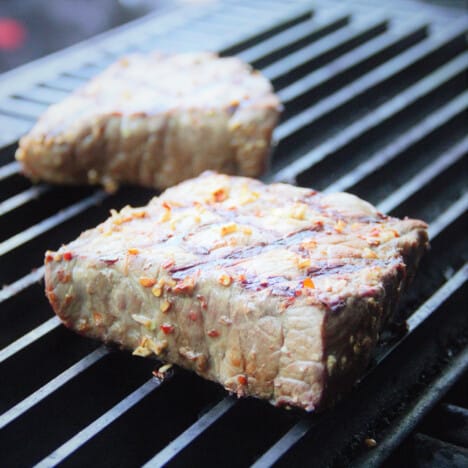 Two seasoned steaks cooking on a grill top.