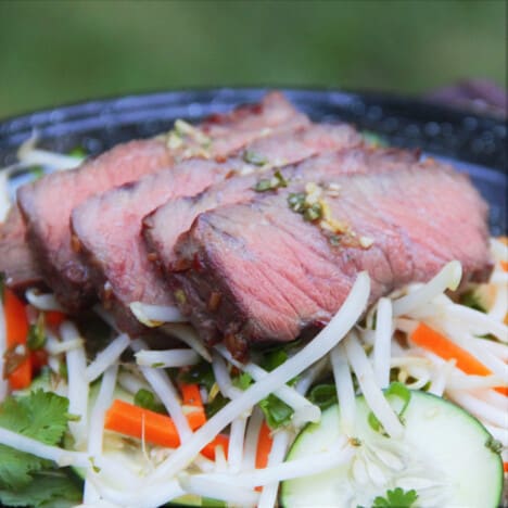 Slices of medium-rare steak are resting on top of a bean sprout, carrot, and cucumber salad.