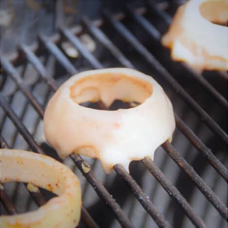 Close up of beer-battered onion rings cooking on a grill.
