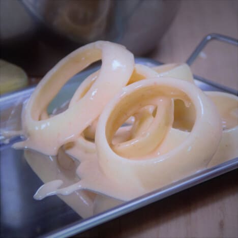 A tray of battered onion rings ready to be placed on the grill.