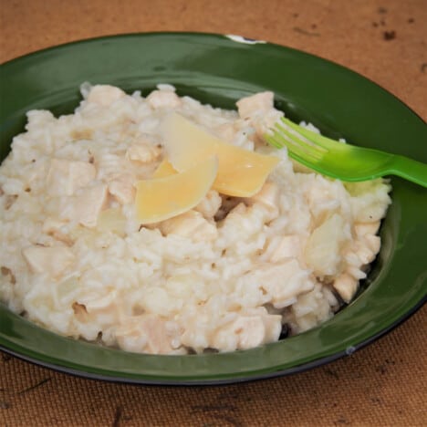 A shallow green bowl holds a serving of Campfire Mock Risotto garnished with chunks of Parmesan cheese.