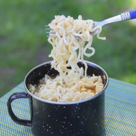 Looking down into a black camping mug filled with ramen noodles being lifted by a fork.