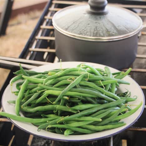 Blanched green beans on a plate on a gas stove with a pot in the background.