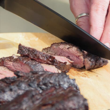 A grilled hanger steak being sliced against the grain on a wooden chopping board.