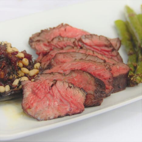 A rare hanger steak sliced and served on a white plate with sides.