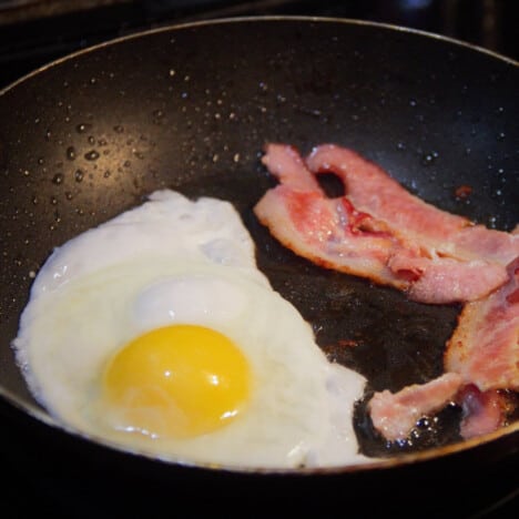 Bacon and eggs cooking in a skillet getting ready to go in a muffin breakfast sandwich.
