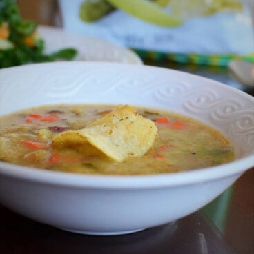The dill pickle and potato chips soup is in a shallow white bowl, garnished with a potato chip.