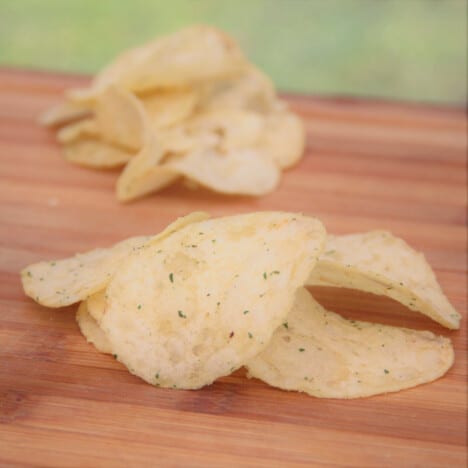 Dill pickle-flavored chips sit in a pile on a wooden cutting board.