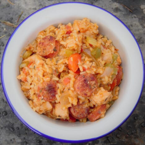 Looking down on a white camp bowl filled with jambalaya highlighting the rich colors and sliced sausage.