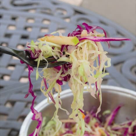 A fork of apple slaw being served from a large bowl.