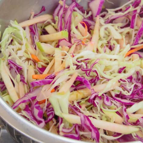 A close up of shredded red and green cabbage, apples, and carrots in a stainless steel bowl.