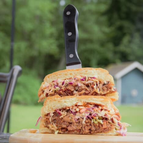 A pulled pork sandwich is sitting ready to be eaten with a knife through it.