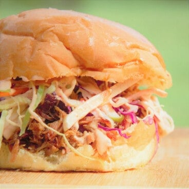 A finished pulled pork sandwich sits on a wooden cutting board.