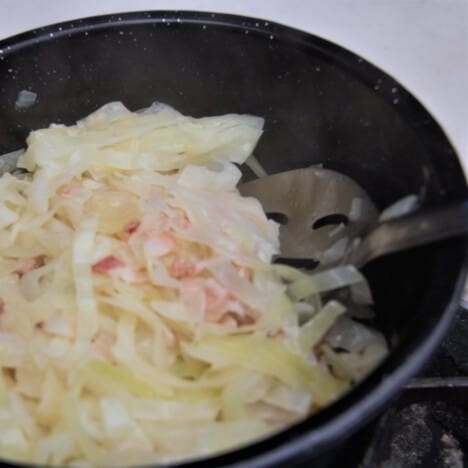 Bacon and cabbage are cooked together in a cast iron skillet.