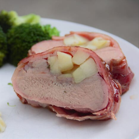 Sliced Bacon Wrapped Tenderloin served on a white plate next to cooked broccoli and ready to eat.