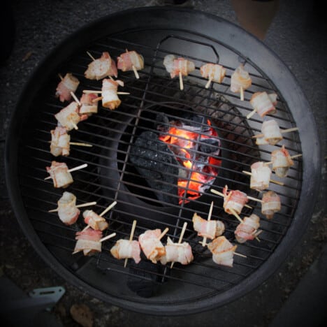 A ring of raw bacon-wrapped shrimp sit in a circular grill.