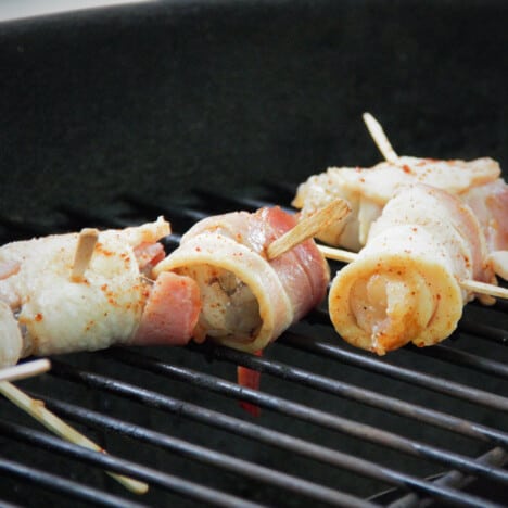 Raw bacon-wrapped shrimp, held together with toothpicks, sit on a grill.