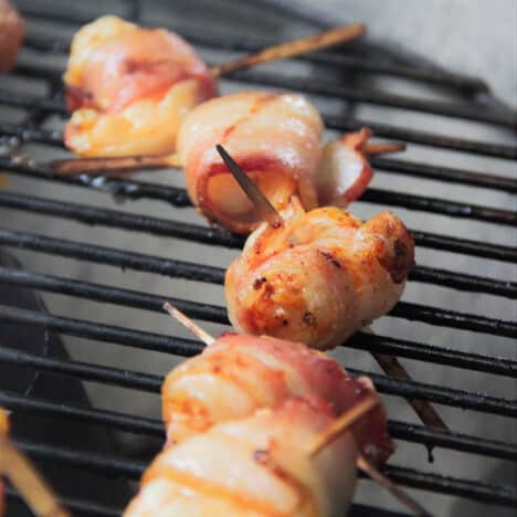 Bacon-wrapped shrimp are skewered with toothpicks and on a grill grate.
