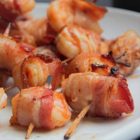 A pile of bacon-wrapped shrimp with toothpicks sits on a white serving plate.