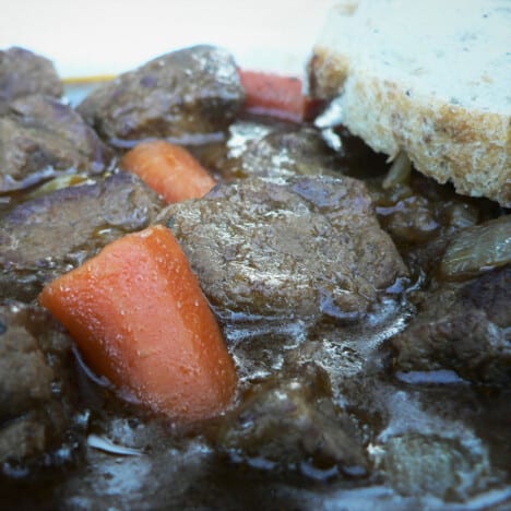 A close up of beef and Guinness stew, with large chunks for carrots and beef in a thick sauce.