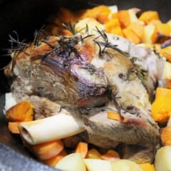 A close up of a roasted leg of lamb resting on roasted pumpkin and potatoes.