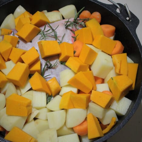 Cubed root vegetables cover a leg of lamb in a Dutch oven ready to be roasted.