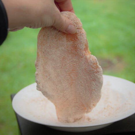 Chicken breast being dusted in the seasoned flour mixture.