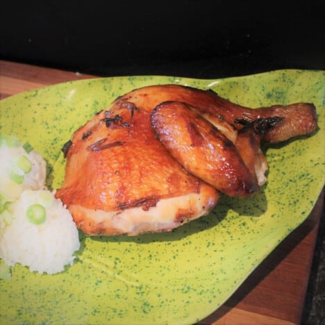 A smoked and grilled quarter of chicken is serve on a green platter with a side of rice.