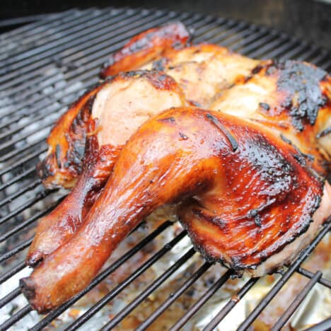 A mahogany colored smoked chicken is on the barbecue cooked and ready to be taken off and served.